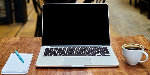 Laptop mit Notizblock und Kaffee